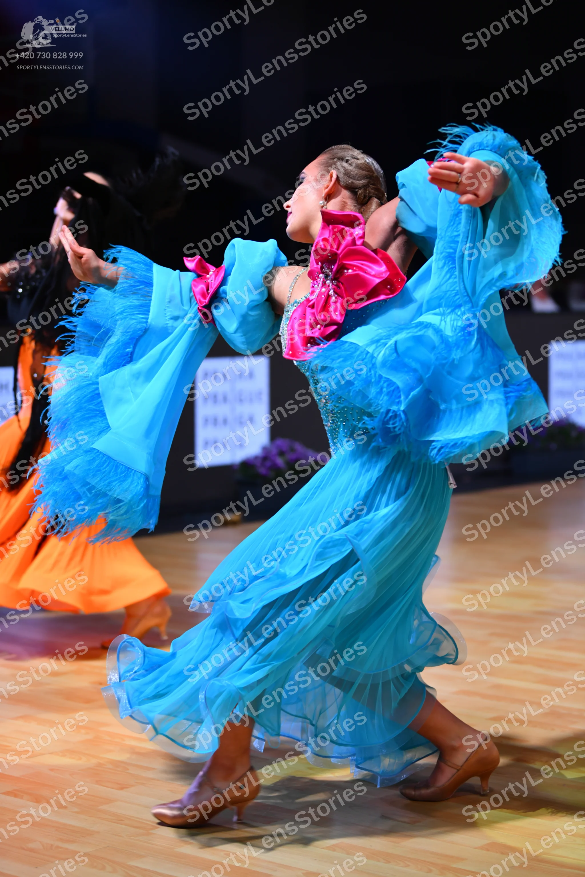 Dancesport competitor: Female dancer: bright blue flowing dress with large, voluminous sheer sleeves, a