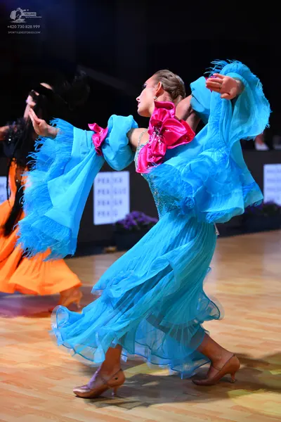 Dancesport competitor: Female dancer: bright blue flowing dress with large, voluminous sheer sleeves, a