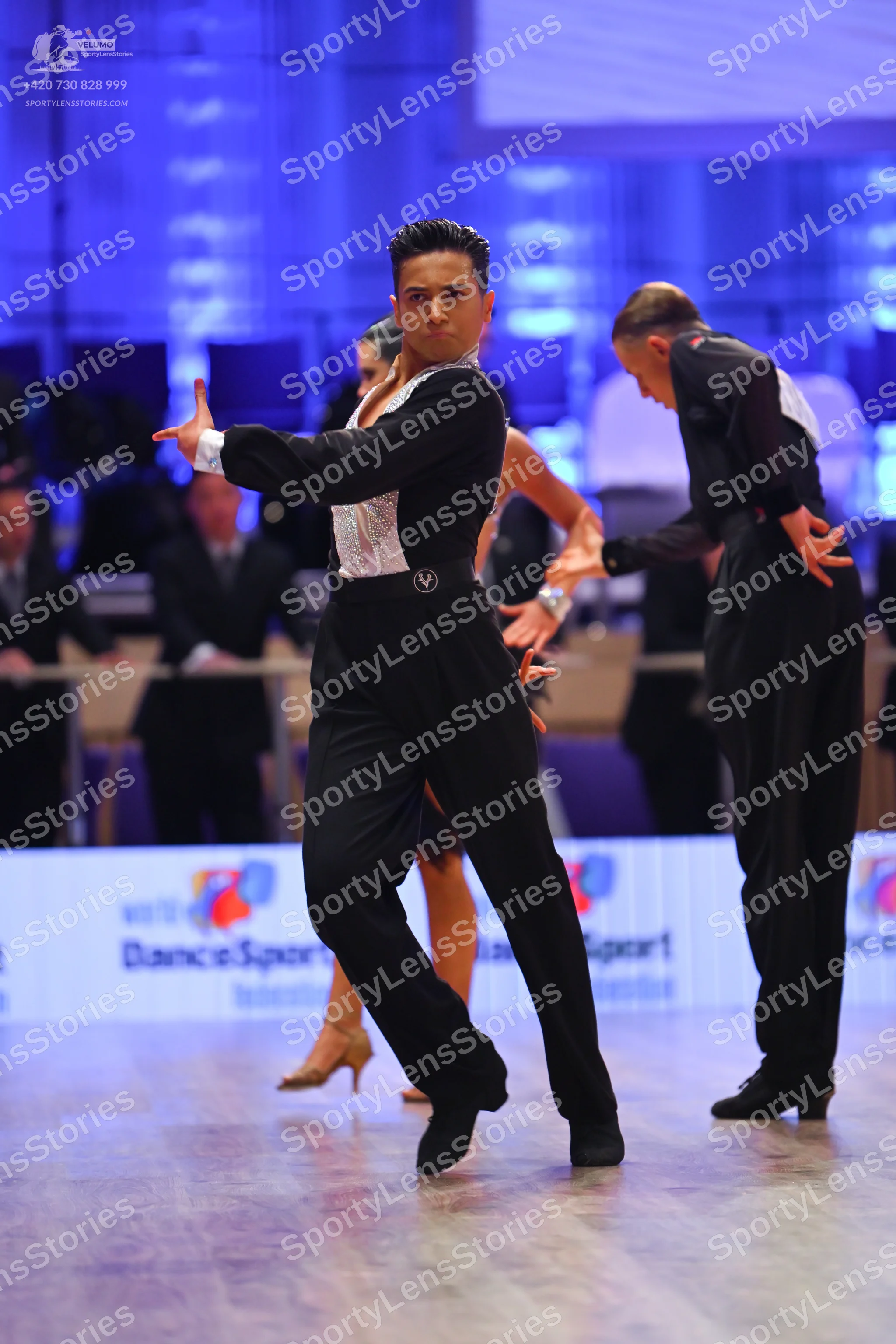 Dancesport competitor: Male dancer in foreground: black Latin dance shirt with a large white textured o