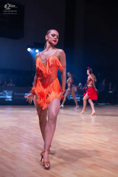 Dancesport competitor: Female dancer in foreground: orange/copper Latin dress with sequins and long fri