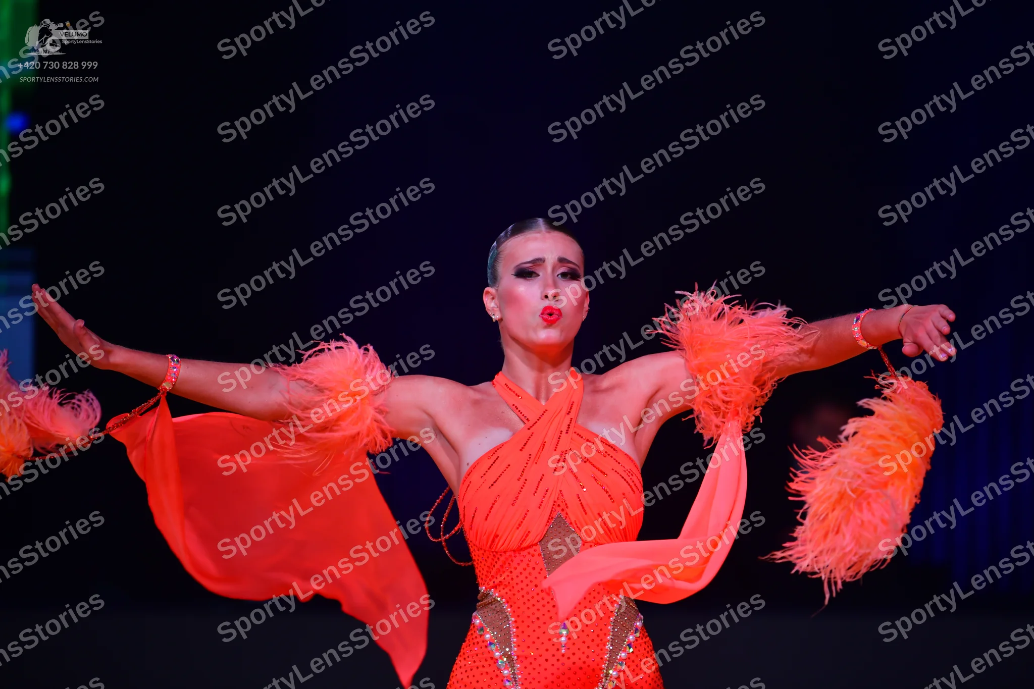 Dancesport competitor: Female dancer: orange latin dress with feathery, flowing fabric on the arms, fea