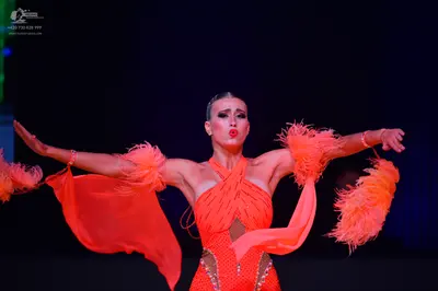 Dancesport competitor: Female dancer: orange latin dress with feathery, flowing fabric on the arms, fea