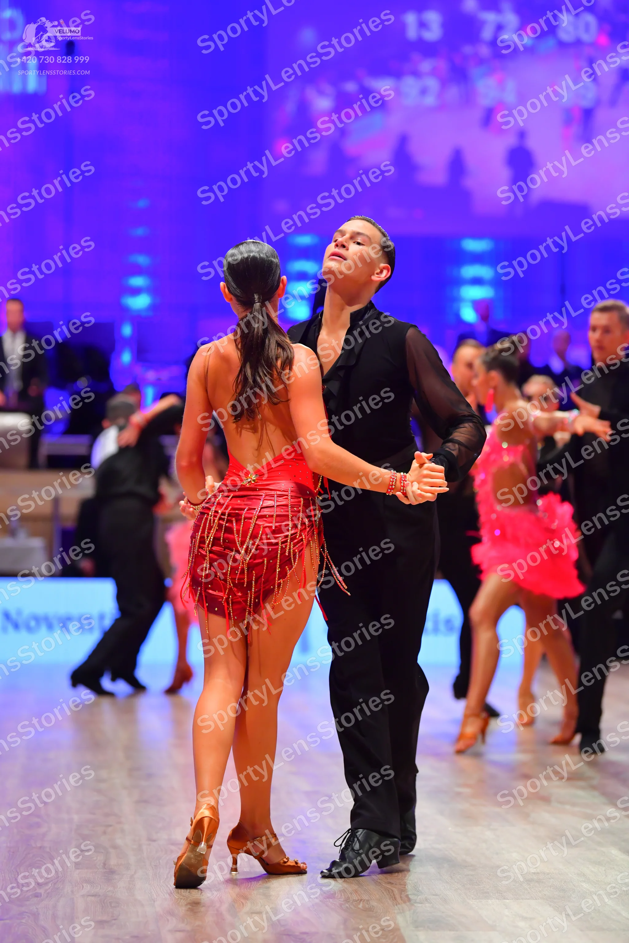 Dancesport competitor: Female dancer in foreground: red Latin dress with fringe