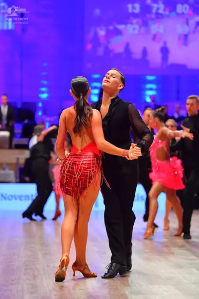 Dancesport competitor: Female dancer in foreground: red Latin dress with fringe