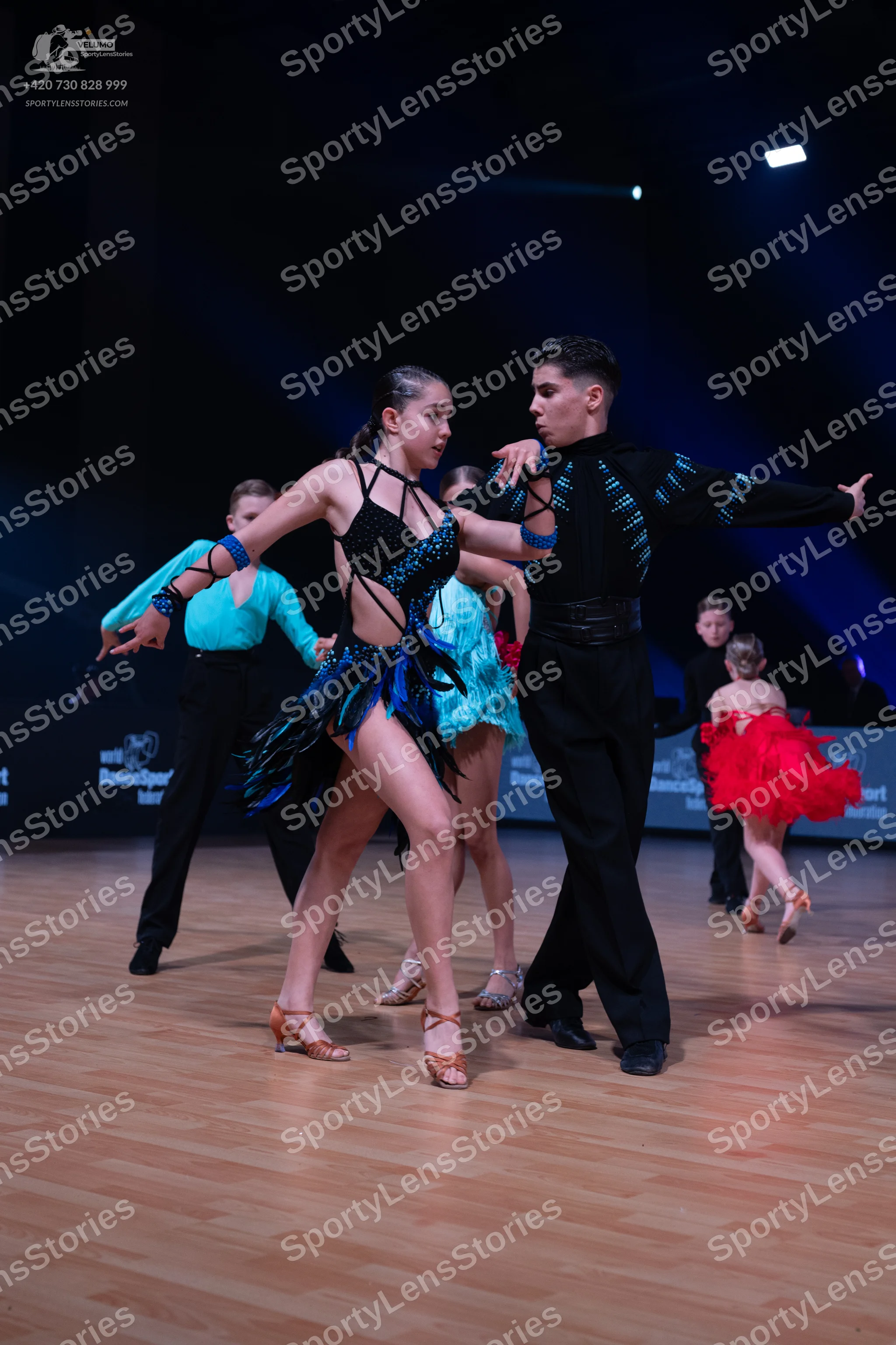 Dancesport competitor: Female dancer in foreground: black Latin dance dress with blue sequin patterns a