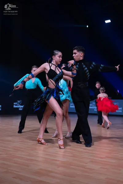 Dancesport competitor: Female dancer in foreground: black Latin dance dress with blue sequin patterns a