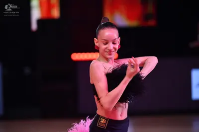 Dancesport competitor: Female dancer: black Latin dance costume with black feathers on the top and pink