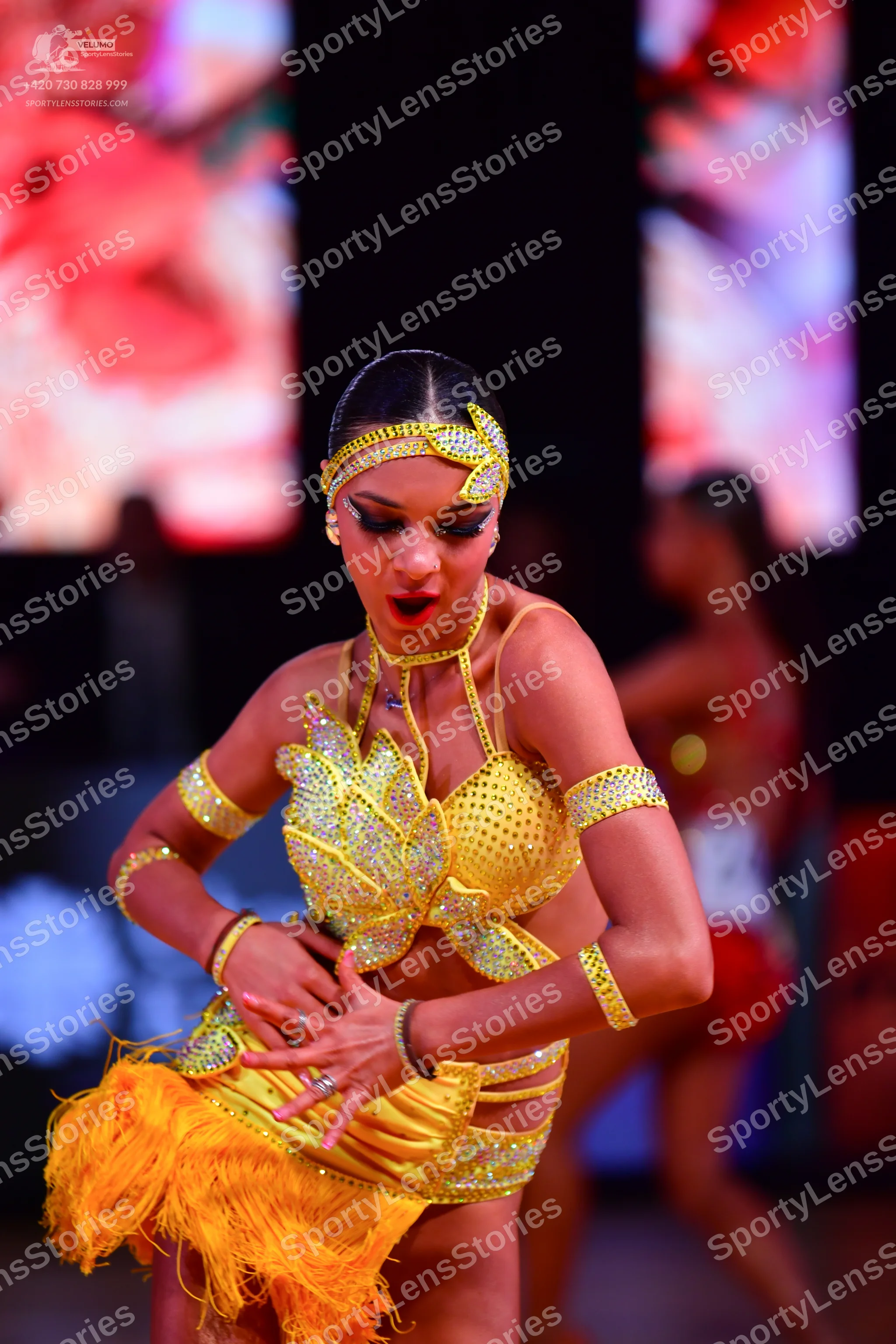 Dancesport competitor: Female dancer in foreground: yellow sequin latin costume with fringe skirt, matc