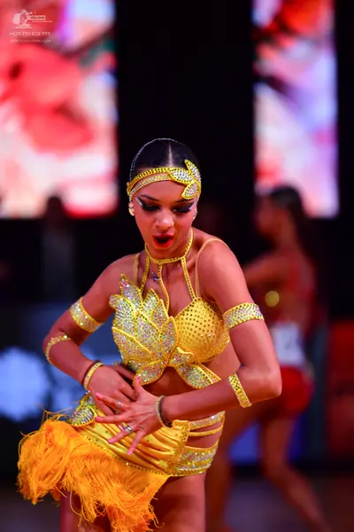 Dancesport competitor: Female dancer in foreground: yellow sequin latin costume with fringe skirt, matc