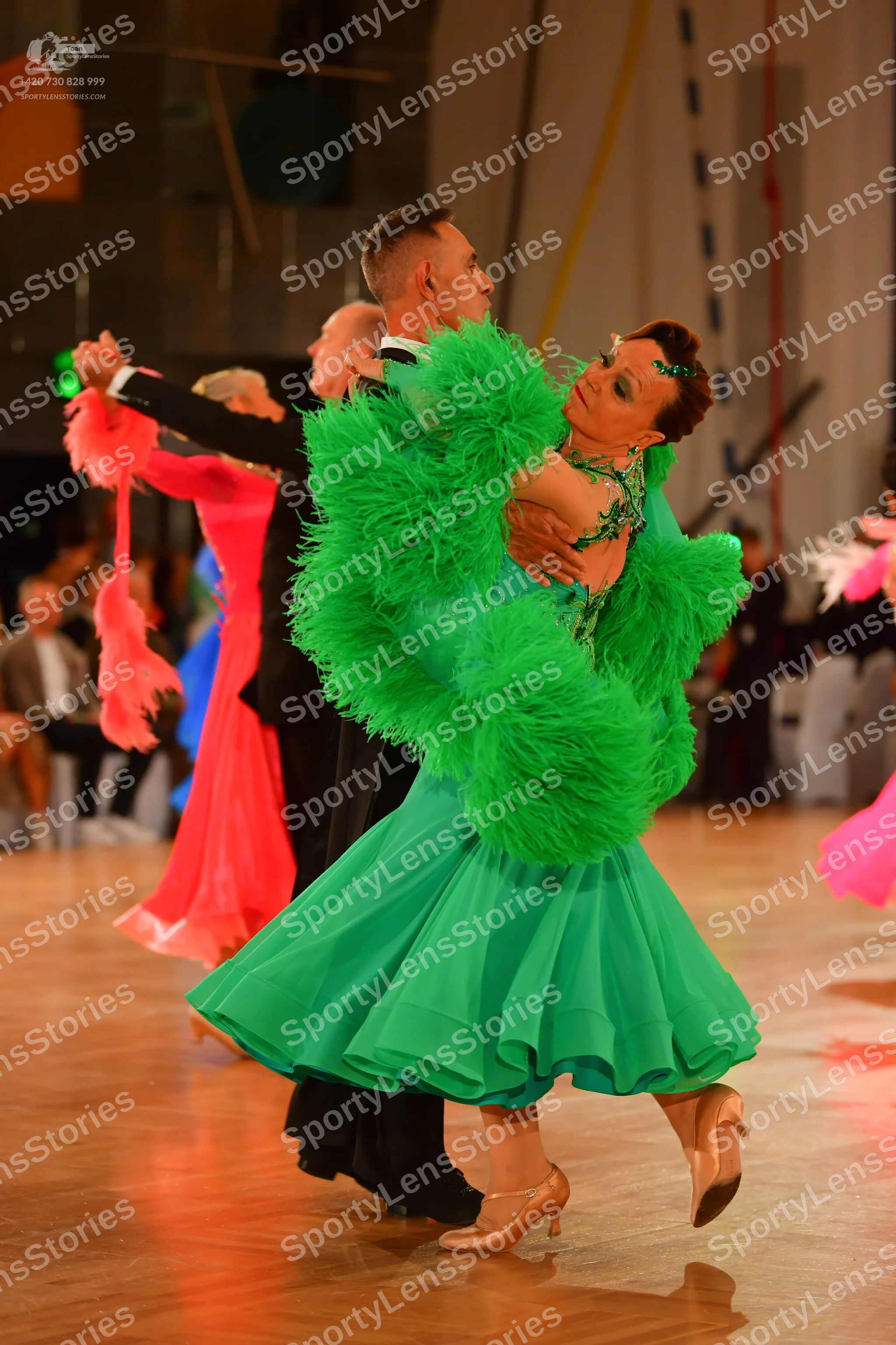 Dancesport competitor: Female dancer in foreground: bright green ballroom dress with large, fluffy gree