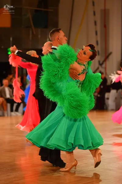 Dancesport competitor: Female dancer in foreground: bright green ballroom dress with large, fluffy gree