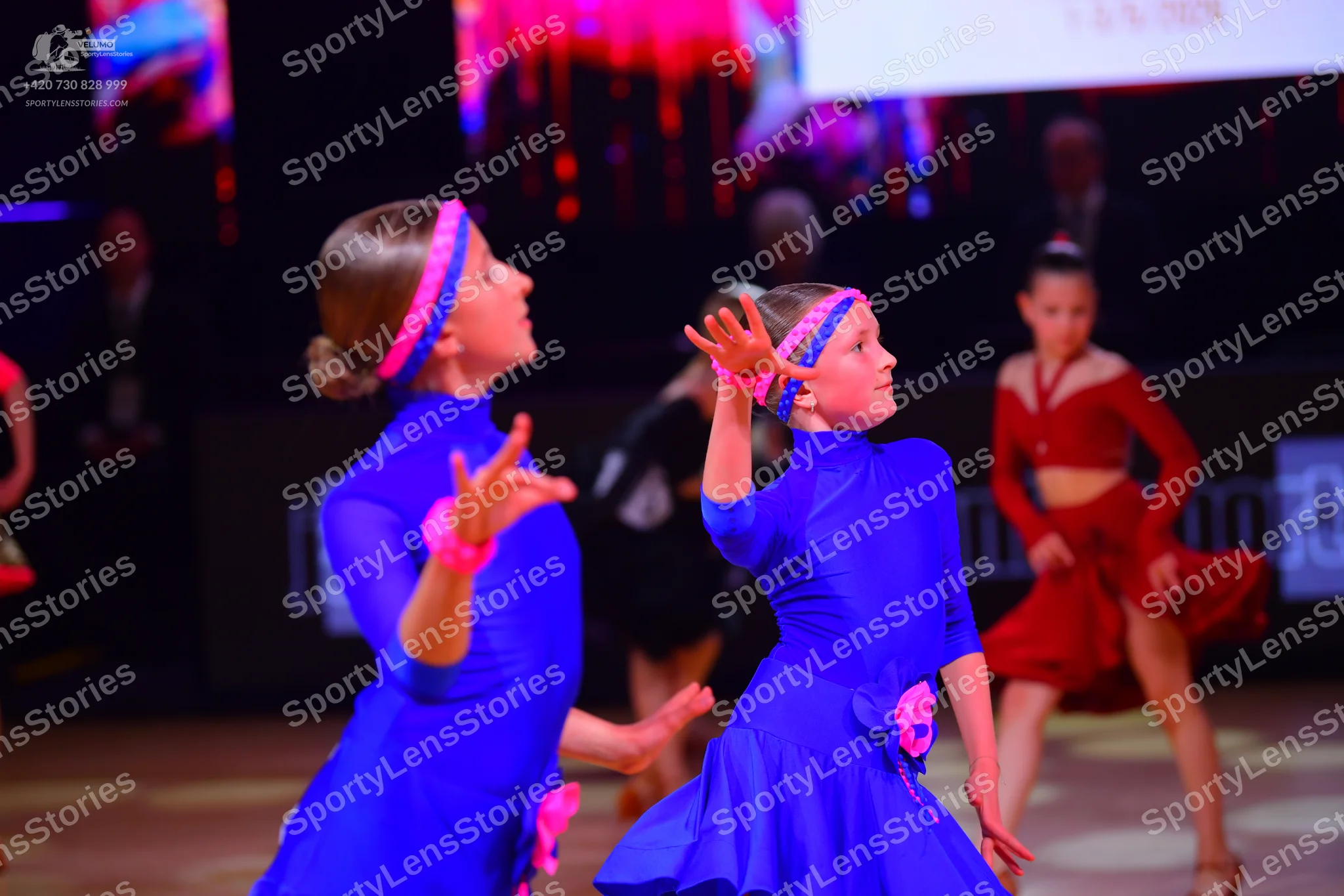 Dancesport competitor: Female dancer (left): blue long-sleeved satin-like dress with a pink headband an