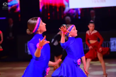 Dancesport competitor: Female dancer (left): blue long-sleeved satin-like dress with a pink headband an
