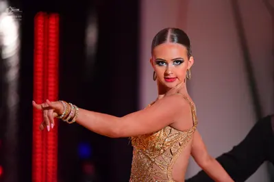Dancesport competitor: Female dancer: gold Latin dance dress with sequins and nude mesh, wearing gold h