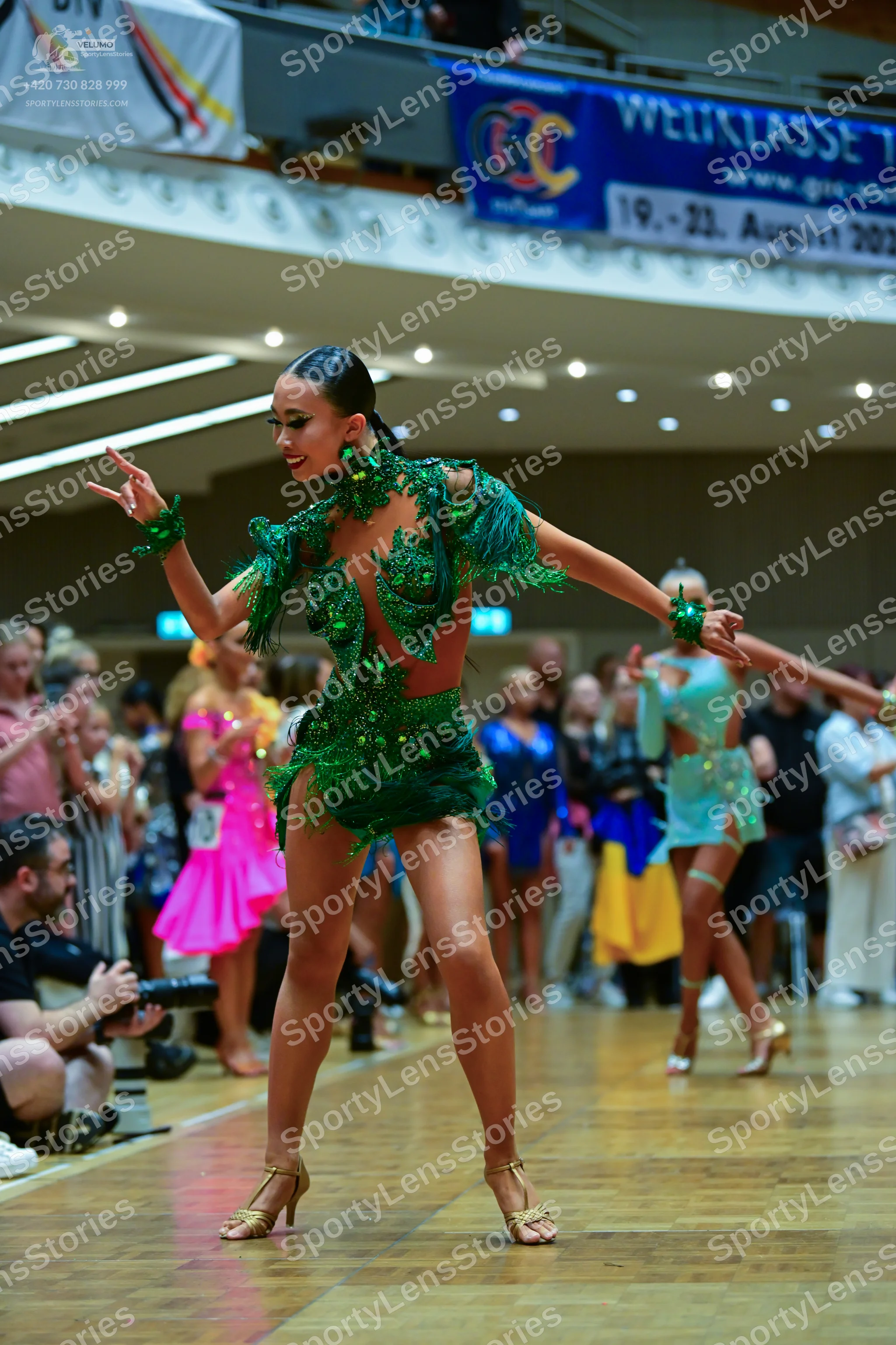 Dancesport competitor: Female dancer in foreground: emerald green latin dress with heavy green sequin e