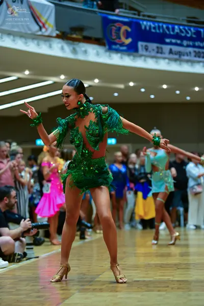 Dancesport competitor: Female dancer in foreground: emerald green latin dress with heavy green sequin e