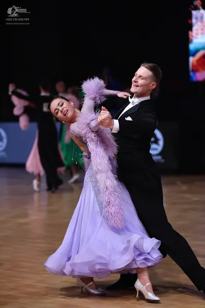 Dancesport competitor: Female dancer: lavender ballgown with a voluminous, ruffled skirt and a large, f