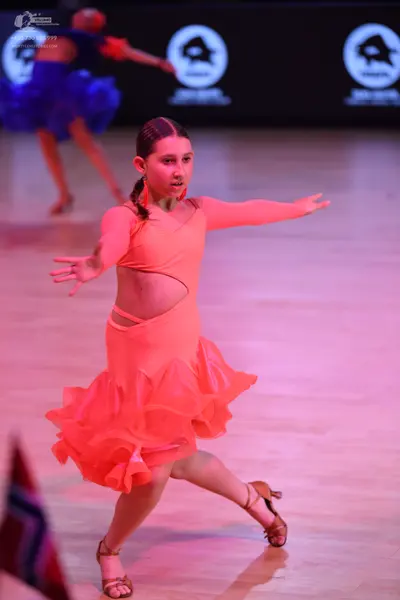 Dancesport competitor: Female dancer in foreground: peach-colored long-sleeved latin dress with side cu