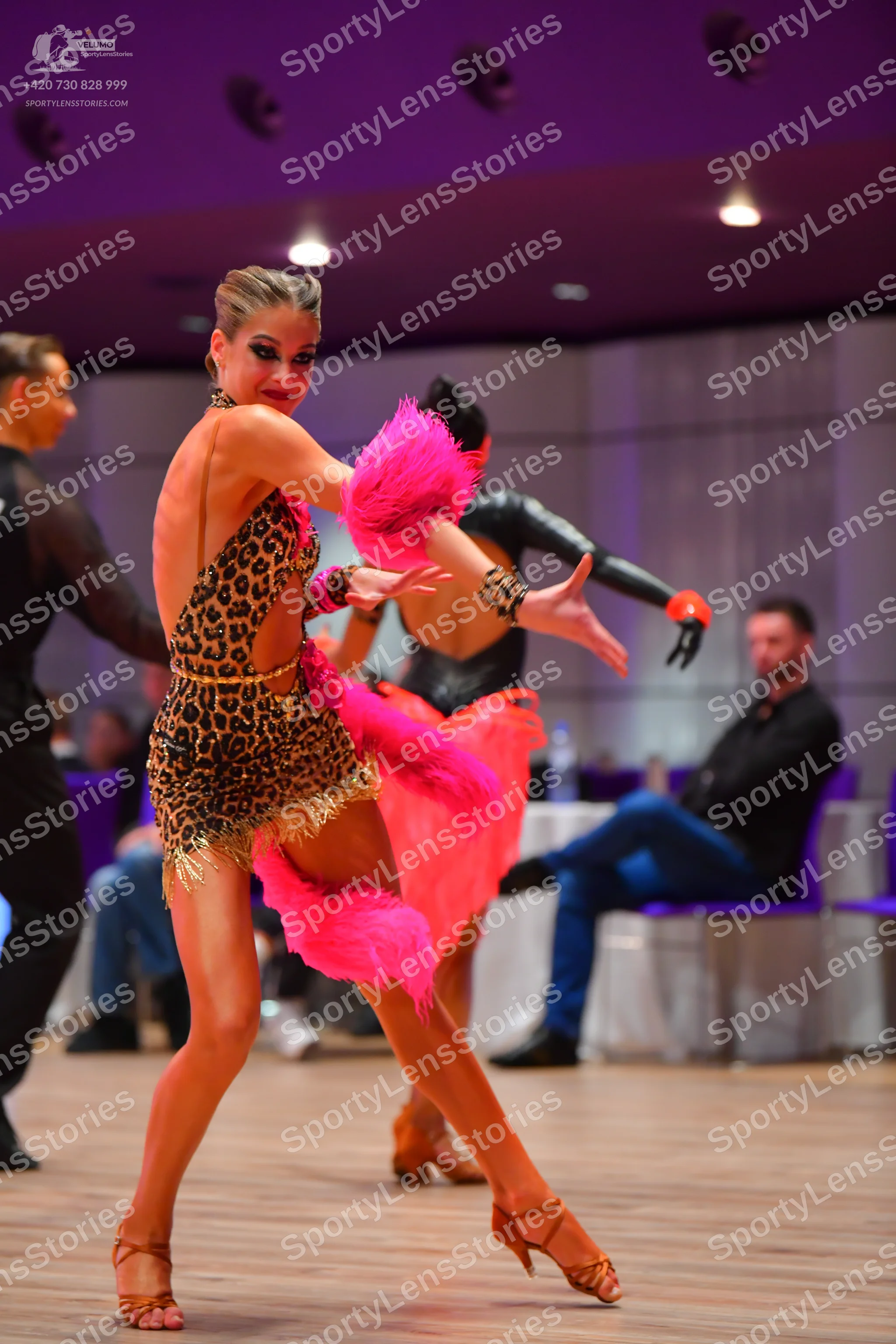 Dancesport competitor: Female dancer (foreground): leopard print Latin dress with gold fringe and a lar