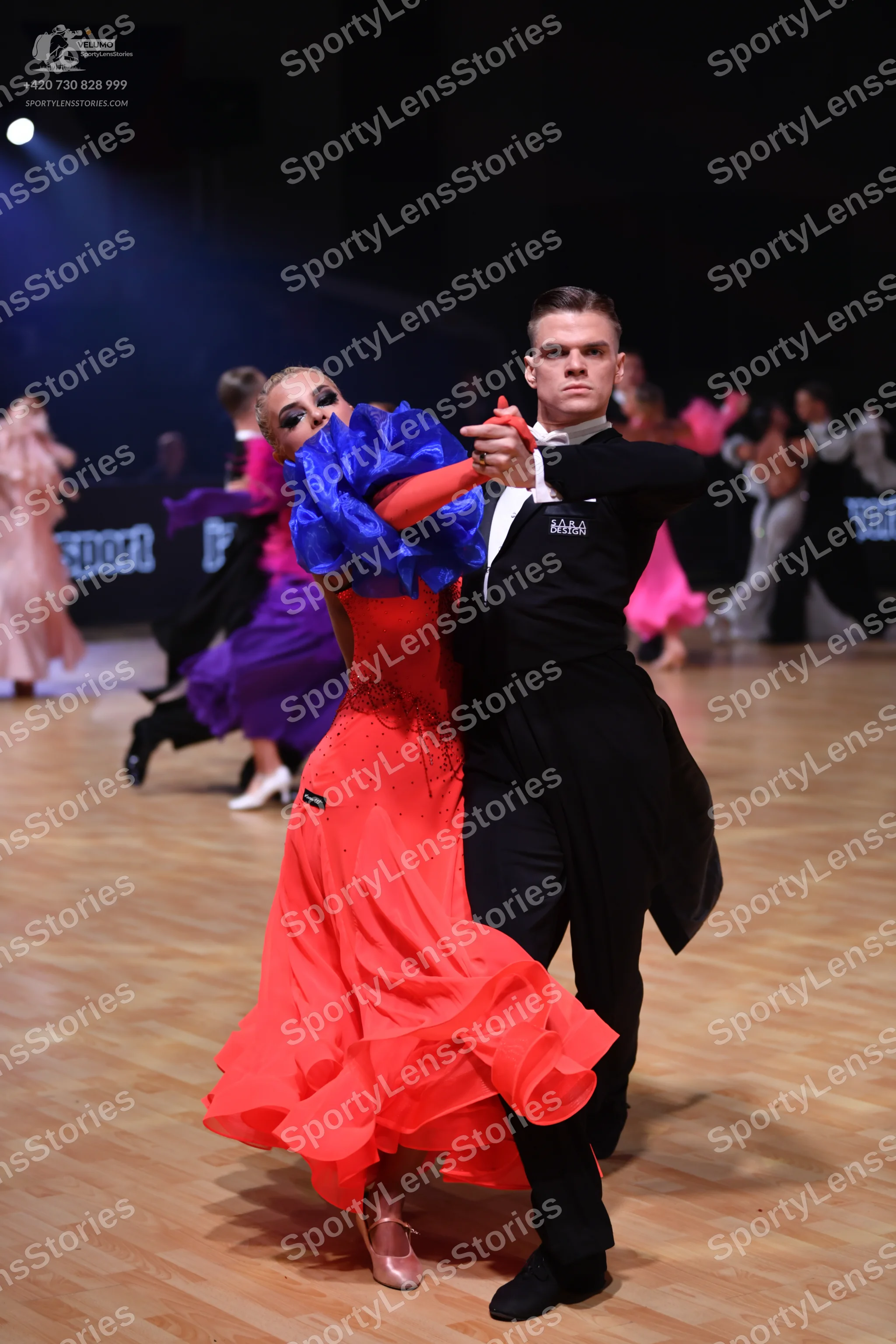 Dancesport competitor: Main female dancer: red ballroom gown with large blue ruffled sleeves and a volu