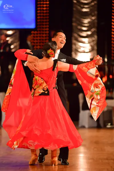 Dancesport competitor: Female dancer: red latin-style dress with large, flowing, patterned sleeves and 