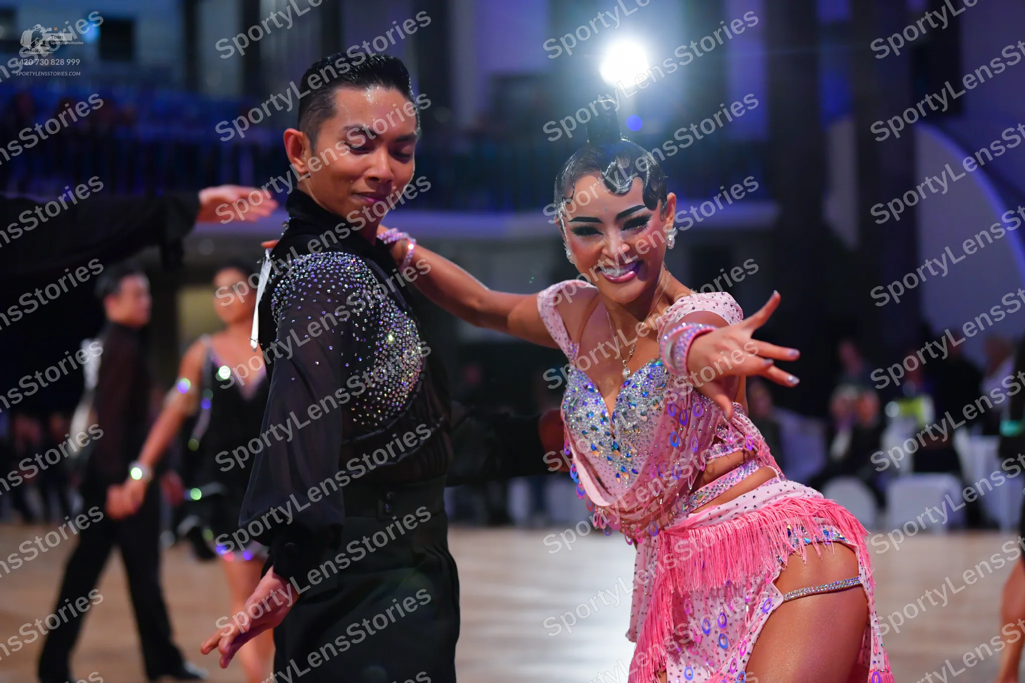 Dancesport competitor: Male dancer in foreground: black long-sleeved shirt with silver sequins on the c