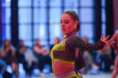 Dancesport competitor: Female dancer: black Latin crop top with gold/yellow sequins and gold fringe, an