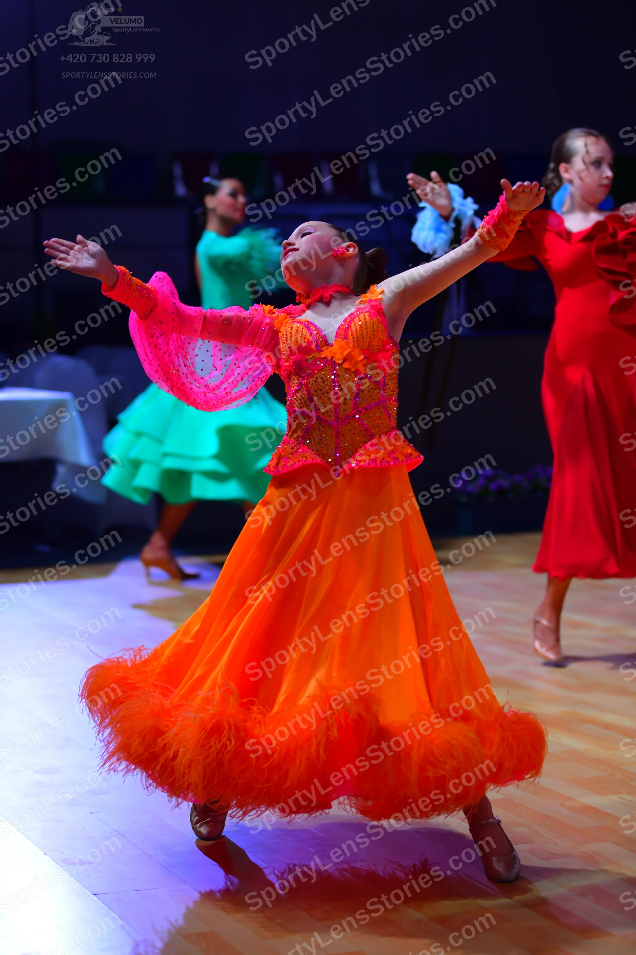 Dancesport competitor: Female dancer in foreground: vibrant orange and pink ballroom gown with a detail