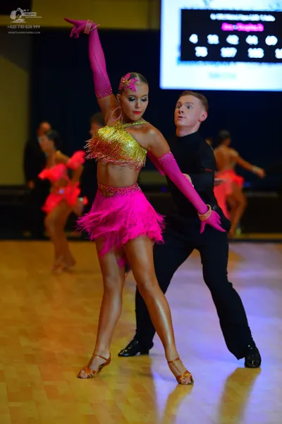 Dancesport competitor: Main female dancer: bright pink and gold Latin costume featuring a gold sequined