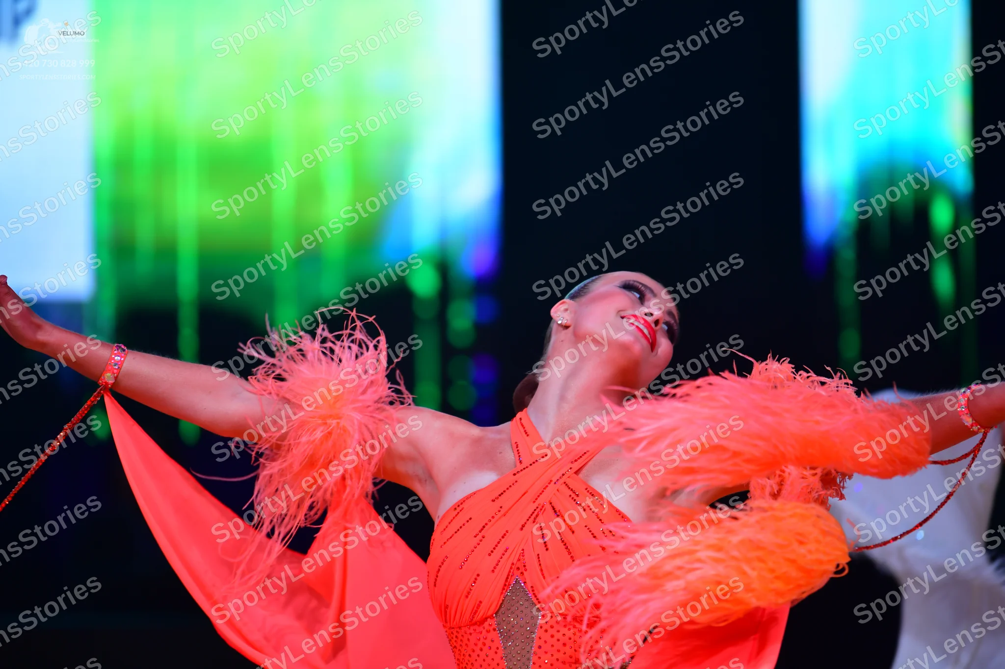 Dancesport competitor: Female dancer: orange Latin dress with large feather accents on the sleeves and