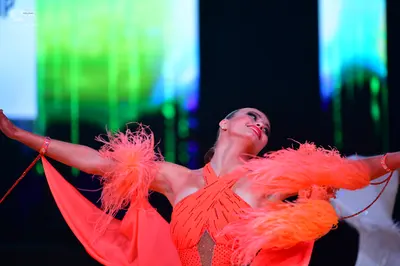 Dancesport competitor: Female dancer: orange Latin dress with large feather accents on the sleeves and 
