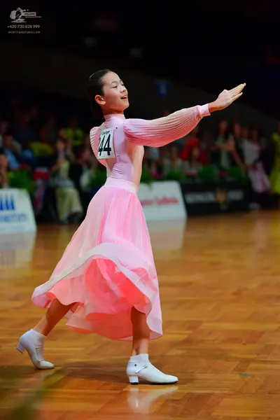 Dancesport competitor: Female dancer: pink long-sleeved ballroom dress with a flowing, layered skirt