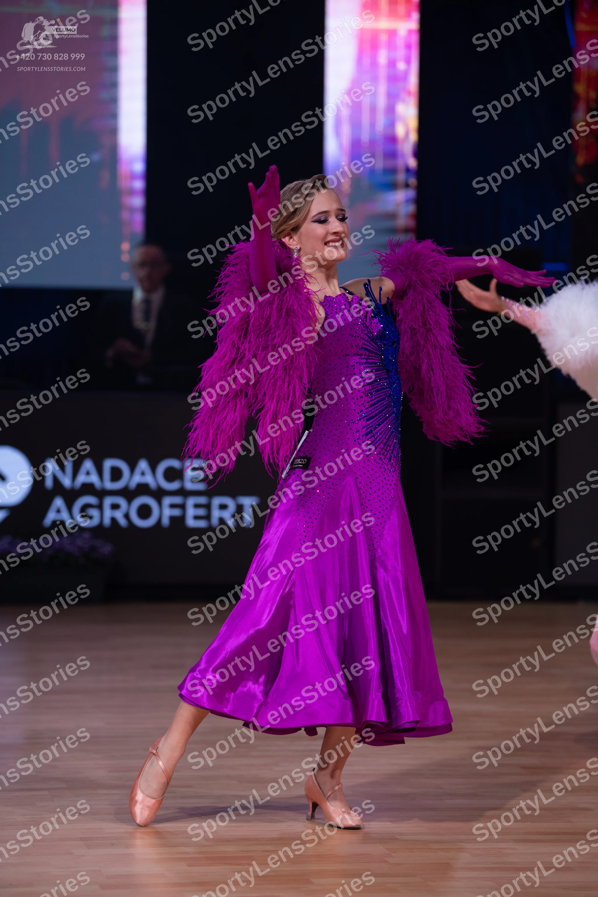 Dancesport competitor: Female dancer: purple satin ballroom dress with large purple feather trim on the