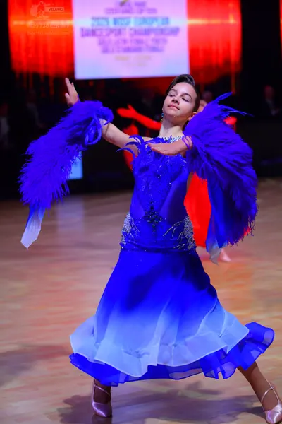 Dancesport competitor: Female dancer: deep blue ballroom dress with large, voluminous blue feather slee