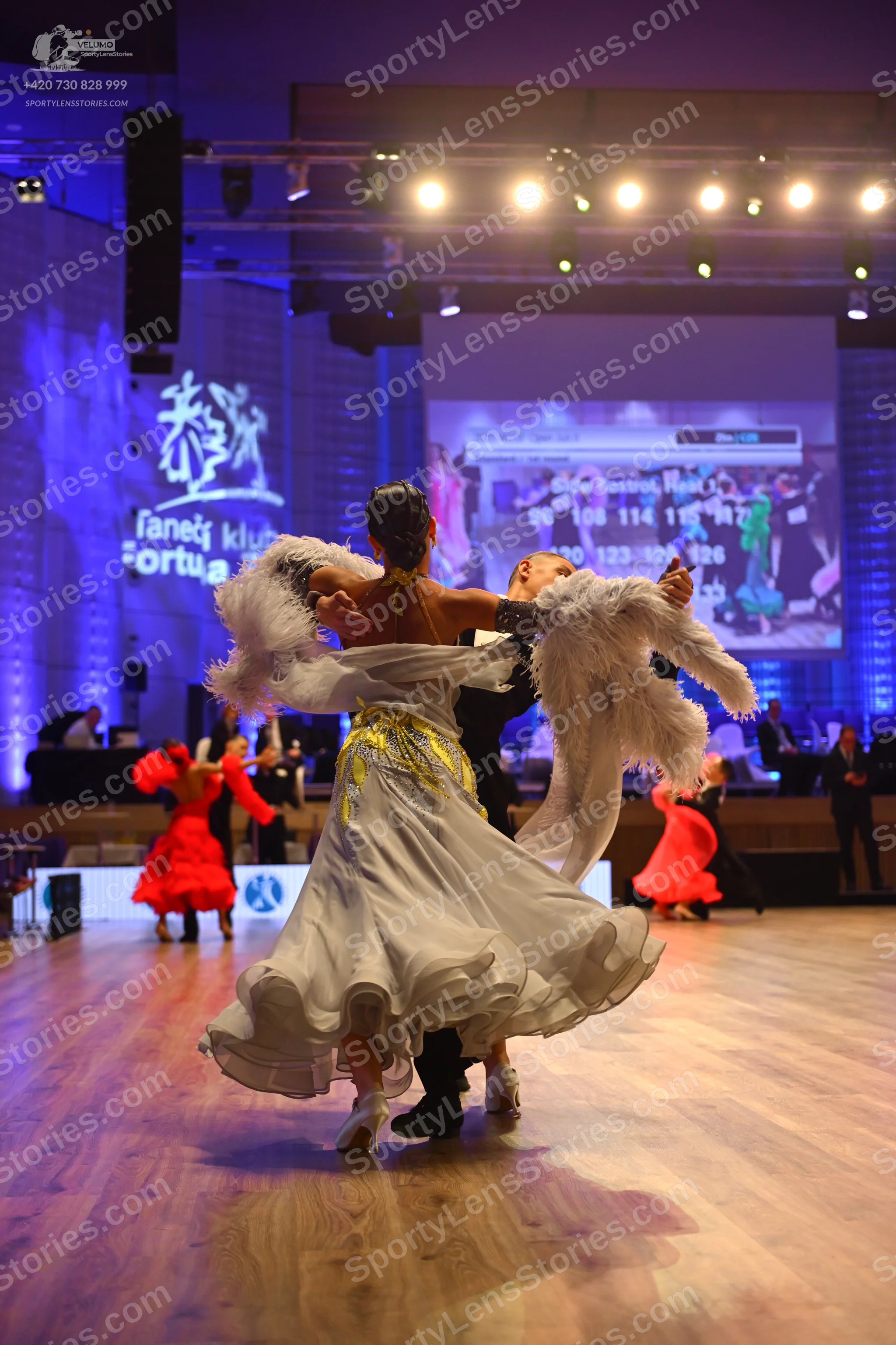 Dancesport competitor: Female dancer: white ballgown with a voluminous, ruffled skirt and white feather