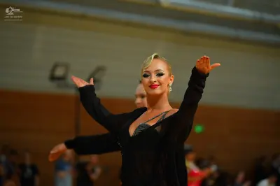 Dancesport competitor: Female dancer: black long-sleeved open-front top over a dark, possibly sequined,