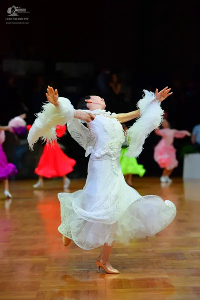 Dancesport competitor: Female dancer in foreground: white lace long-sleeved dress with voluminous ruffl