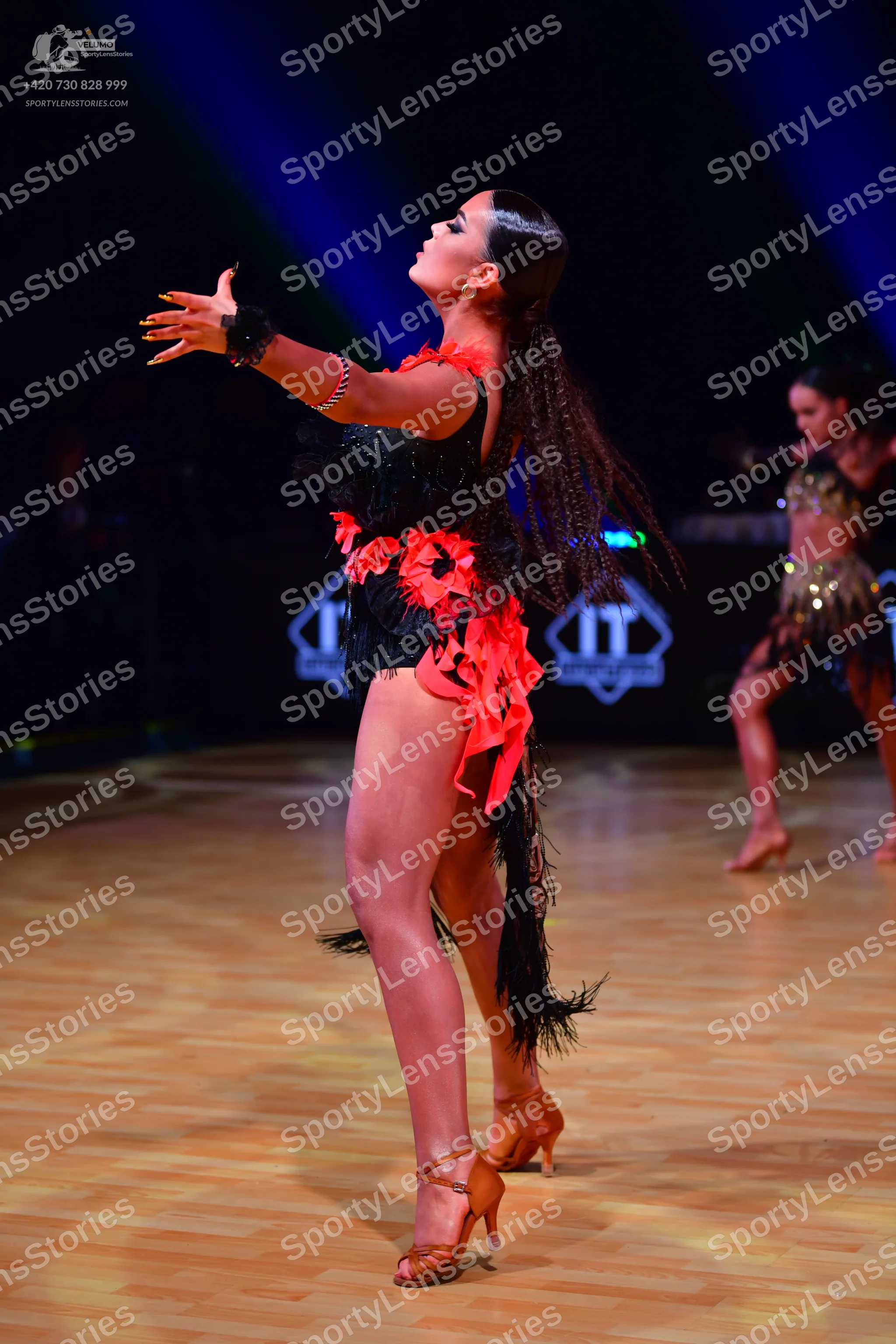 Dancesport competitor: Female dancer in foreground: black and red latin dress with red floral appliques