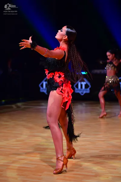Dancesport competitor: Female dancer in foreground: black and red latin dress with red floral appliques