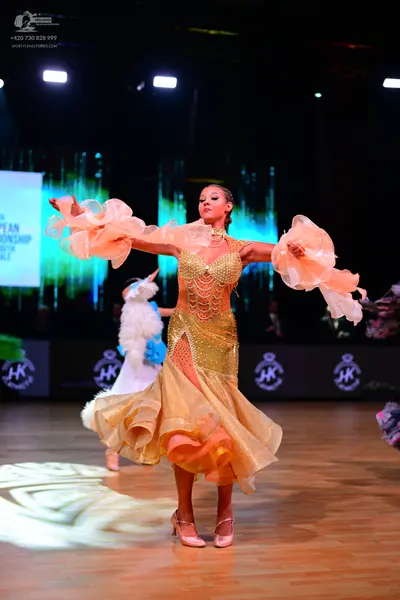 Dancesport competitor: Female dancer: gold latin dress with a sequined bodice and voluminous, ruffled, 