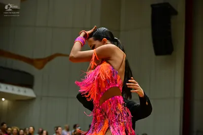 Dancesport competitor: Female dancer: orange, pink, and purple latin dress with heavy fringe and cutout