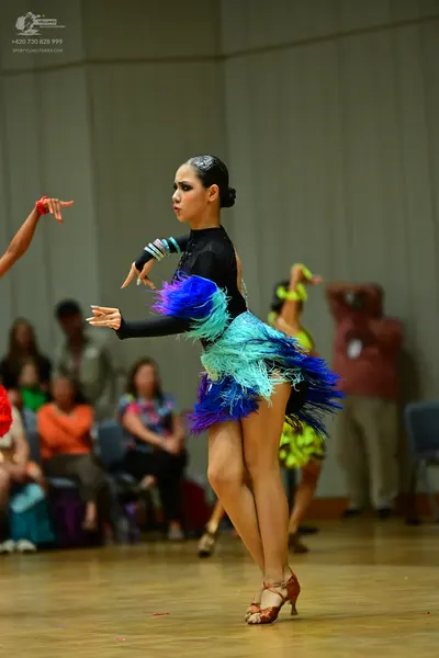 Dancesport competitor: Female dancer in foreground: black long-sleeved Latin dance top with a multi-col