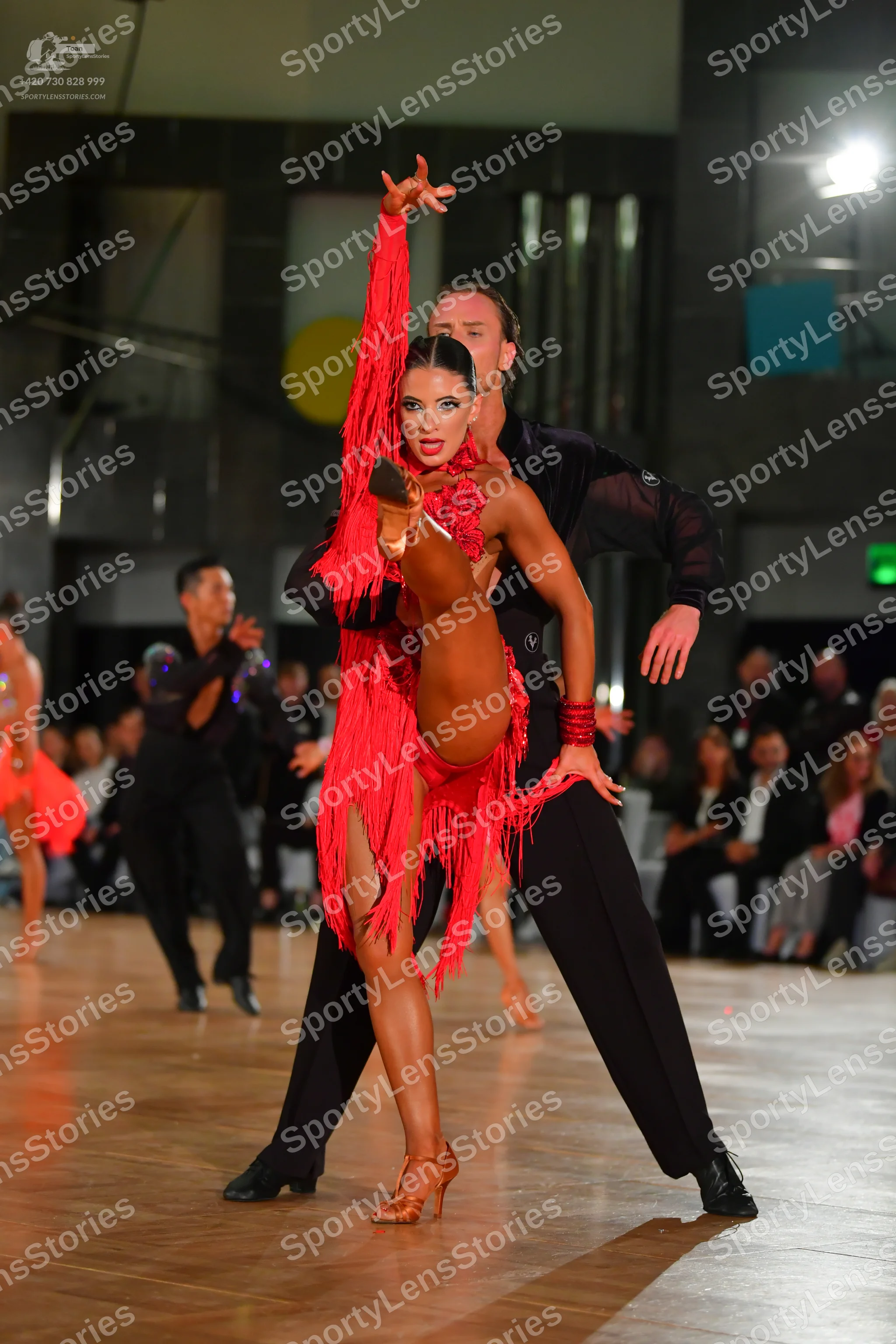 Dancesport competitor: Central female dancer: red latin dress with long fringe and red and gold bracele