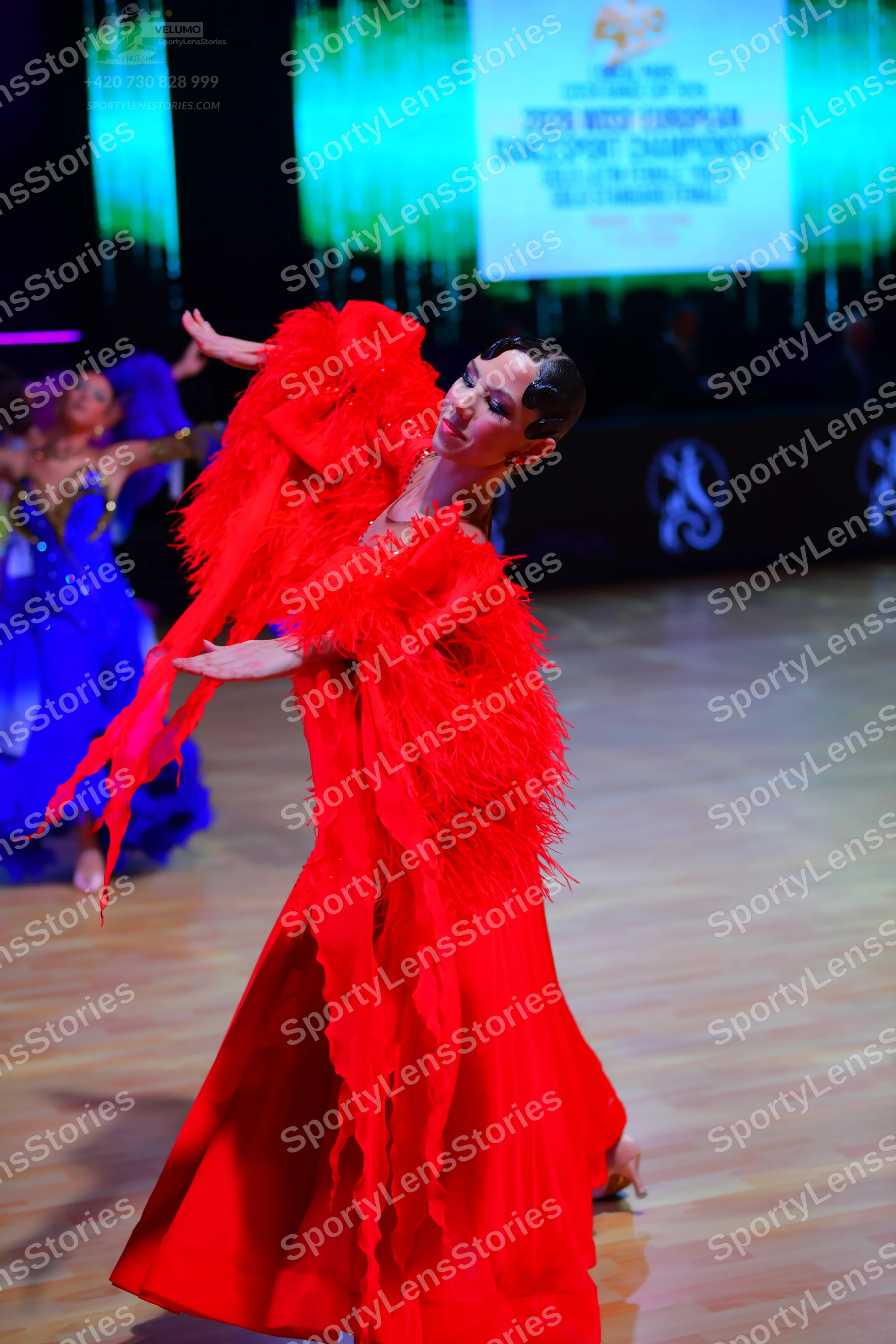 Dancesport competitor: Female dancer in foreground: red ballroom dress with voluminous feather-like tex