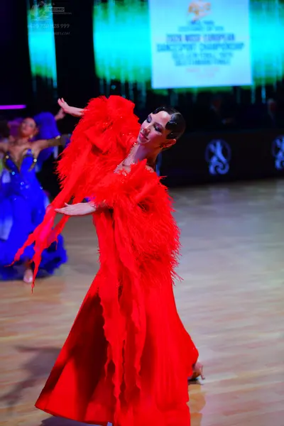 Dancesport competitor: Female dancer in foreground: red ballroom dress with voluminous feather-like tex
