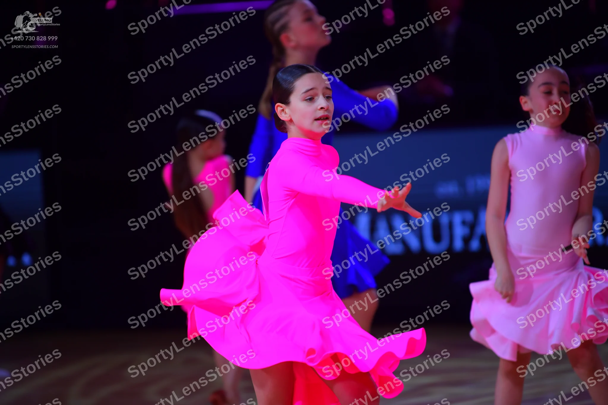 Dancesport competitor: Female dancer in foreground: bright pink long-sleeved Latin dance dress with a f