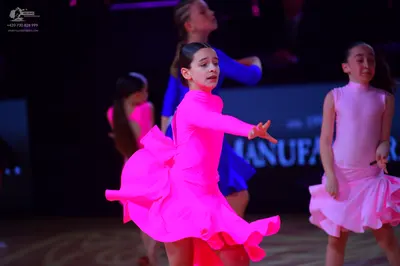 Dancesport competitor: Female dancer in foreground: bright pink long-sleeved Latin dance dress with a f