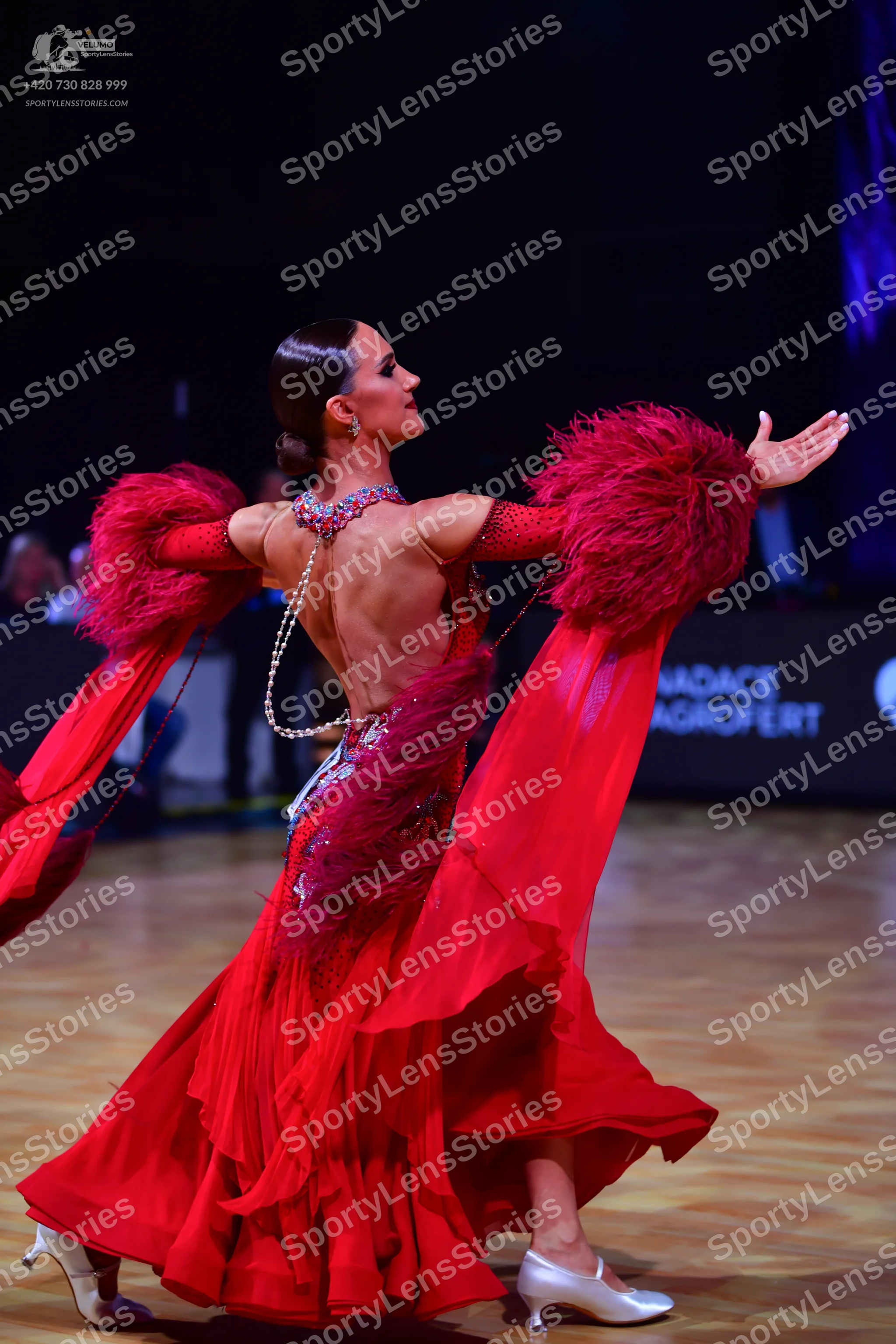 Dancesport competitor: Female dancer: red latin dress with large red feather sleeves, a draped pearl-li