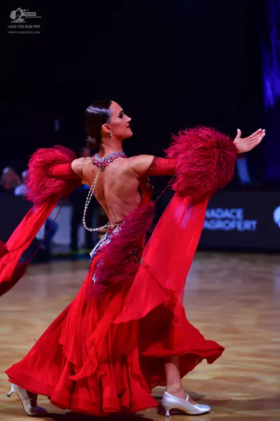 Dancesport competitor: Female dancer: red latin dress with large red feather sleeves, a draped pearl-li