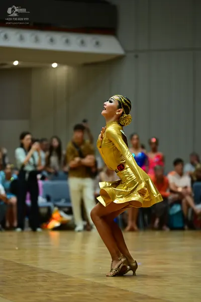 Dancesport competitor: Female dancer: metallic gold Latin dress with a flared skirt, a gold hair access